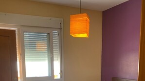 Ein Schlafzimmer mit Bett, Fenster mit Jalousien, einer Pendelleuchte und einer Tür.