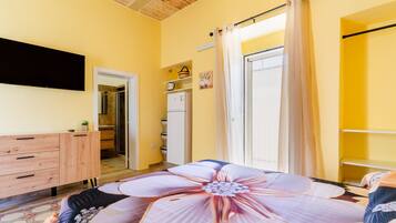 A bedroom with a large bed, a TV mounted on the wall, a wardrobe, and a door leading to a bathroom.