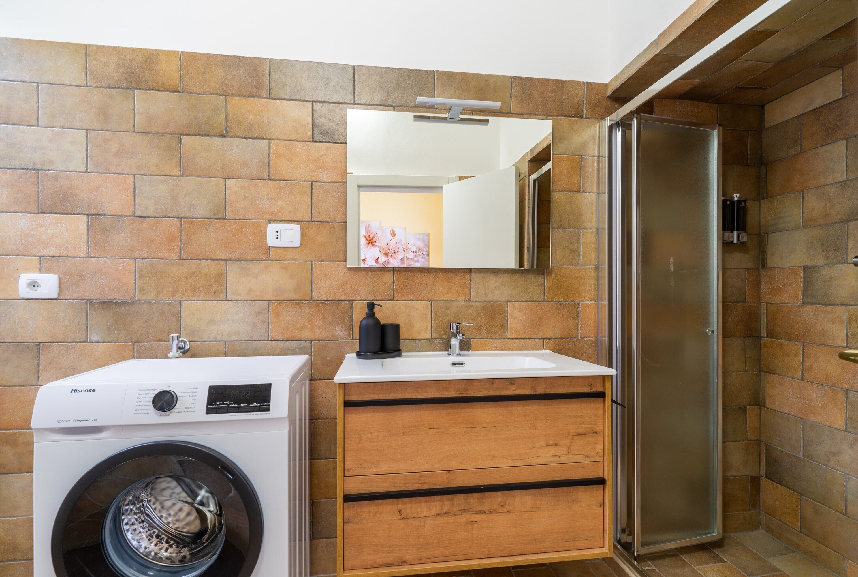 Een kleine badkamer met een wasmachine, een wastafel, een spiegel en een douche.