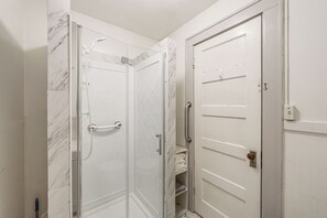 A bathroom with a glass-enclosed shower, a white door with a handle, and a towel rack.