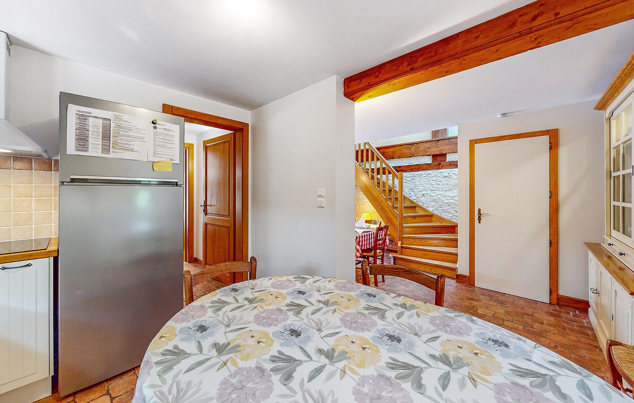 Une pièce de taille modeste comprenant un lit, un réfrigérateur, un escalier en bois et un coin repas avec une table et des chaises.