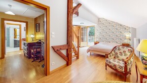 Une pièce spacieuse avec un escalier en bois, un lit recouvert d’un tissu à motifs floraux et une vue sur l’extérieur.
