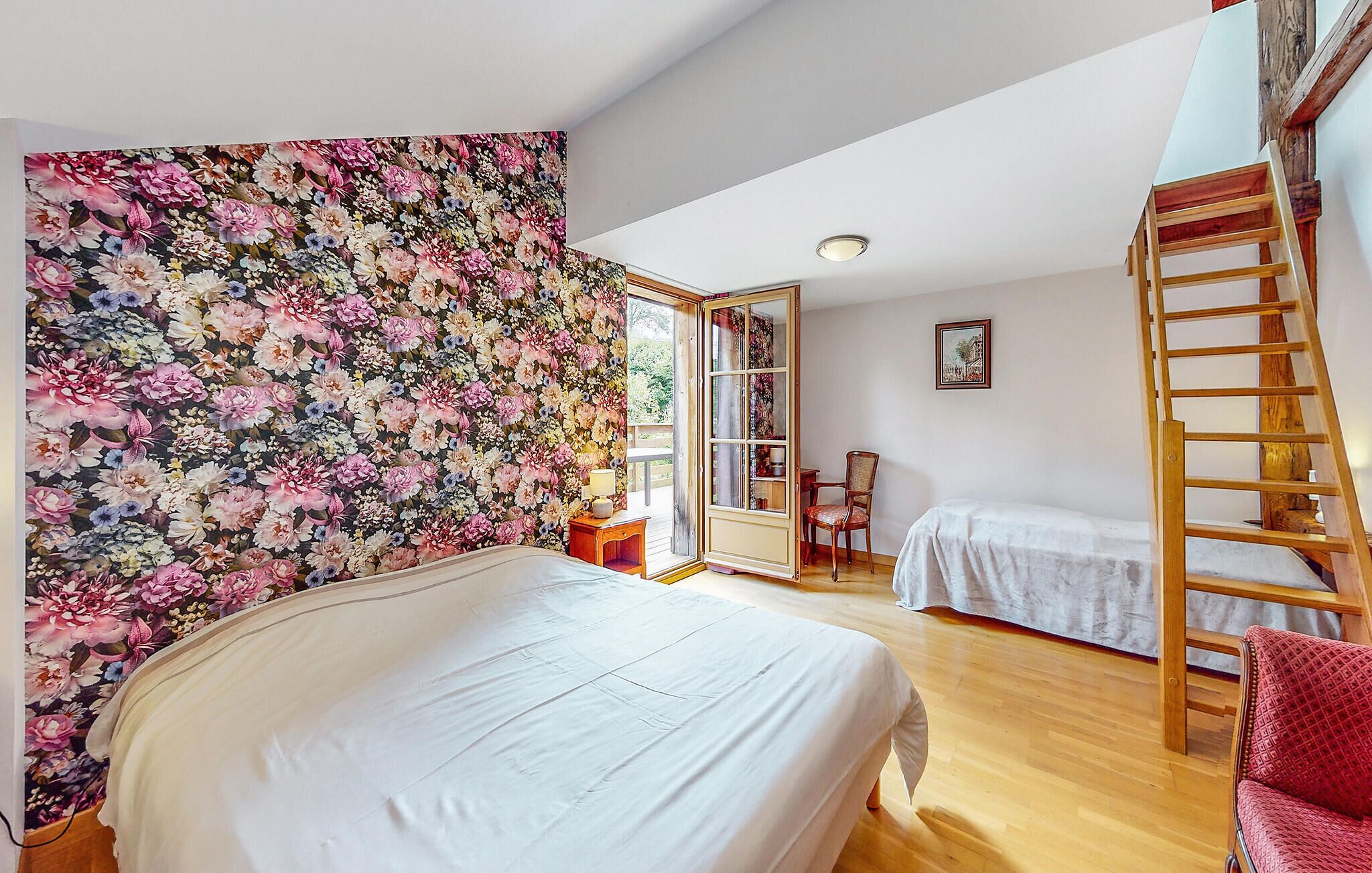 Ein Schlafzimmer mit floraler Tapete, einem Bett, einem Sessel, einer Leiter und einem kleinen Tisch.