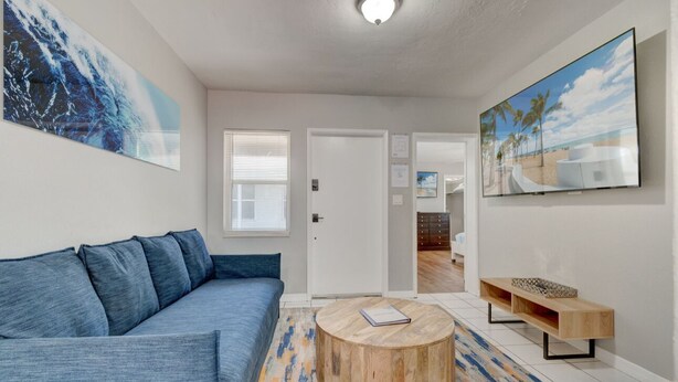 Una sala de estar moderna con un sofá azul, una mesa de centro redonda de madera y un cuadro con motivos playeros en la pared.