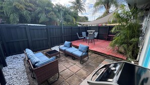 Un patio con mobiliario exterior, una parrilla y una mesa cubierta.