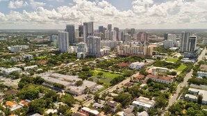 Vista aérea de un paisaje urbano con edificios altos, zonas verdes y una combinación de áreas residenciales y comerciales.