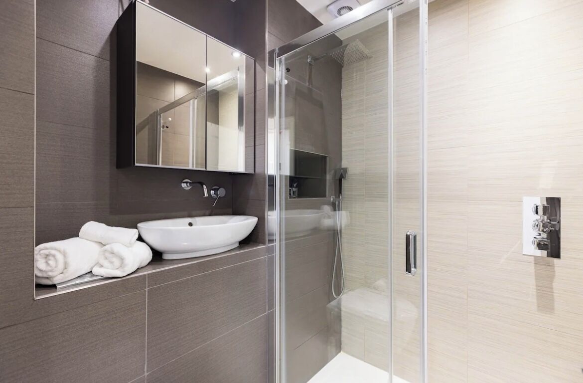 A modern bathroom with a large mirror, a white sink, and a glass-enclosed shower.
