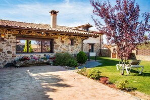 Une maison en pierre avec un toit en tuiles, une allée pavée et une pelouse bien entretenue.
