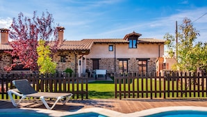 Una casa de piedra con piscina, terraza de madera y patio cercado.