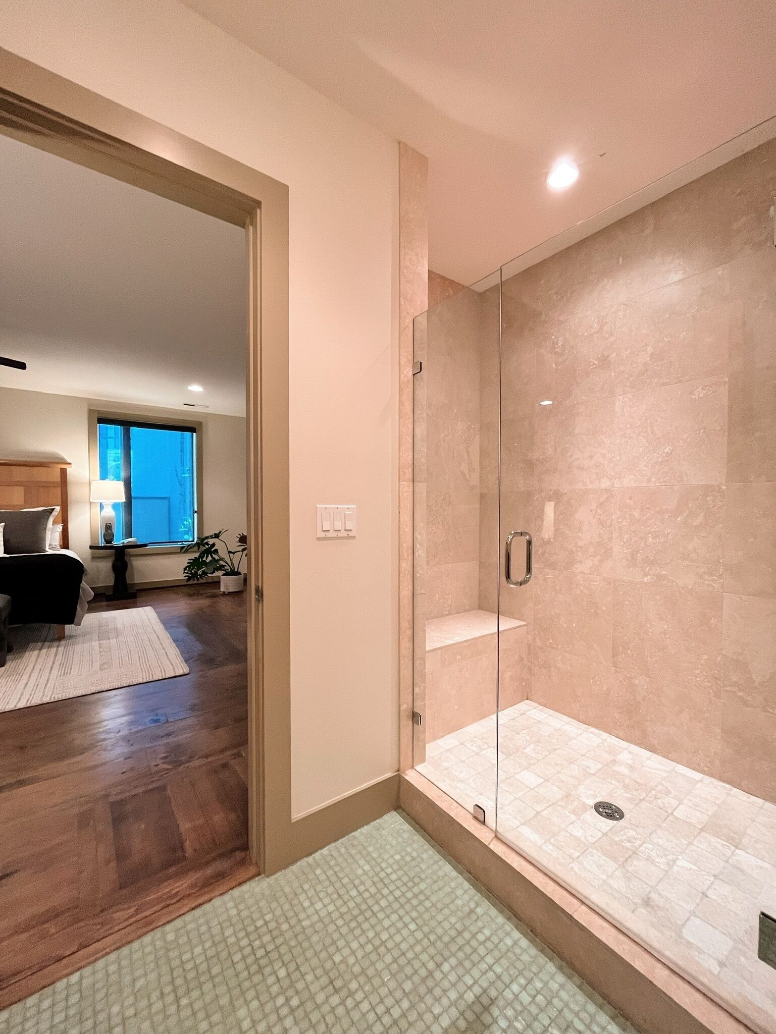A modern bathroom with a glass shower enclosure, a wooden floor, and a visible toilet.