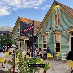 An outdoor seating area with tables and chairs, a sign for 'Cuba Cuba Cafe & Bar', and a building with a green facade and a yellow roof.