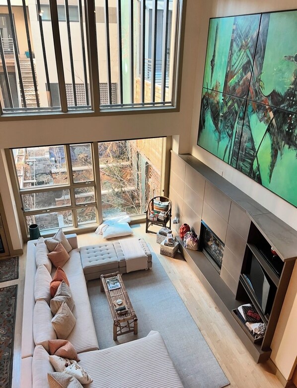 Uma sala de estar moderna com uma TV grande, assentos confortáveis, uma lareira e grandes janelas com vista para a cidade.