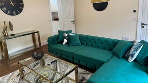Una sala de estar con un sofá verde, una mesa de centro de cristal, un reloj de pared y un adorno en la pared.