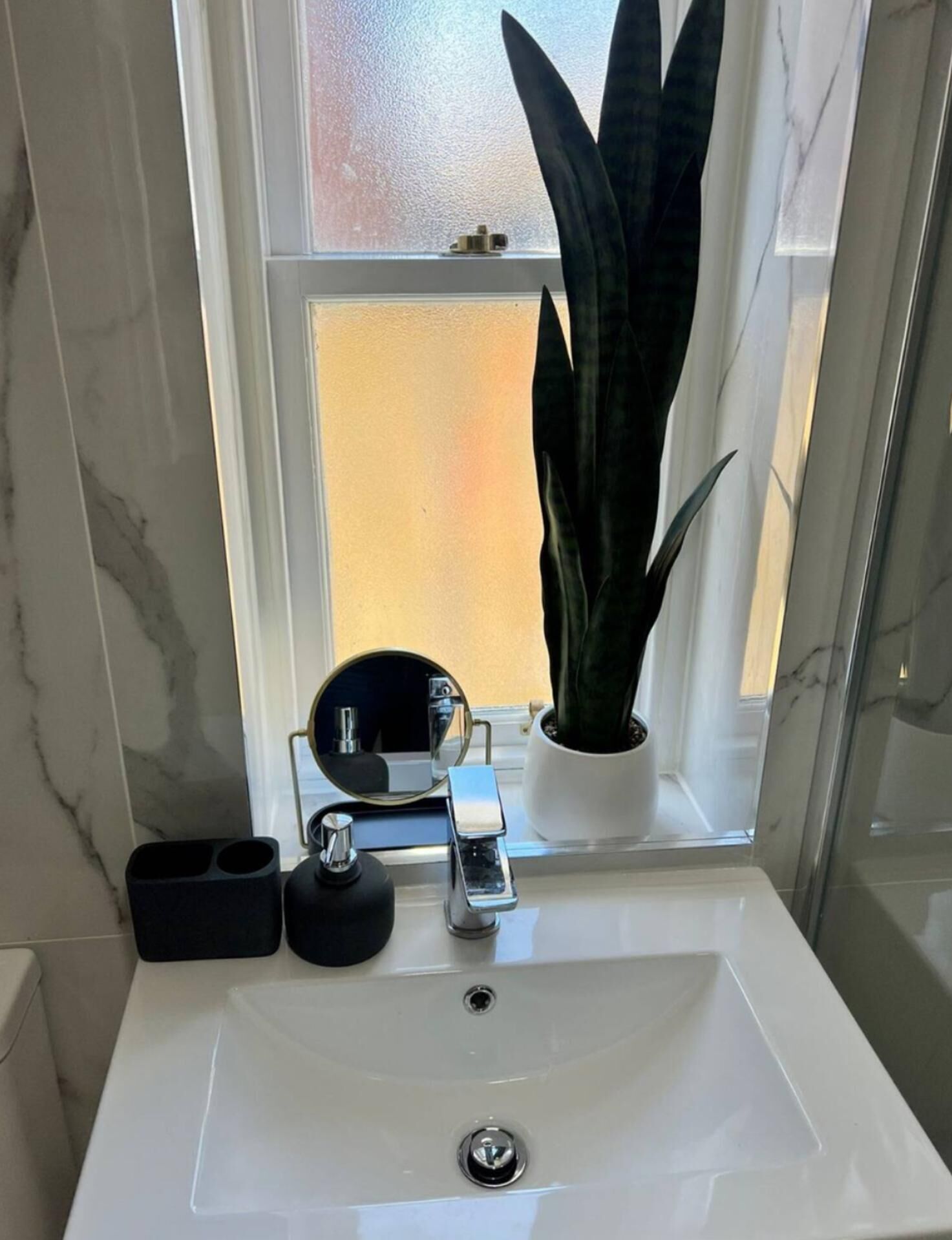 A bathroom with a white sink, a mirror, and a potted plant.