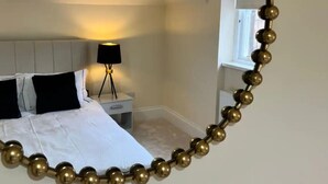 Un dormitorio con cama, mesita de noche, lámpara y una cadena dorada decorativa.