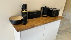 Una encimera de cocina con cubierta de madera, un tazón negro, saleros y pimenteros negros, una cafetera, un recipiente para azúcar, un recipiente para té y un tostador.