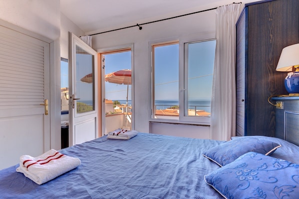 Ein Schlafzimmer mit einem Bett, einem Fenster mit Meerblick und einer Tür.
