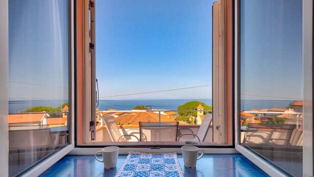 Ein Balkon mit Meerblick, ein Tisch mit zwei Tassen und einer blau-weißen Tischdecke.