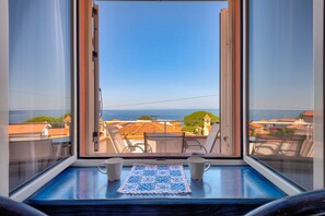 Ein Balkon mit Meerblick, ein Tisch mit zwei Tassen und einer blau-weißen Tischdecke.