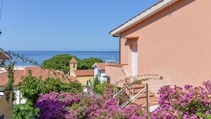 Ein Küstengebäude mit rotem Ziegeldach, einer rosafarbenen Außenwand und Bougainvillea-Blüten in Lila im Vordergrund.