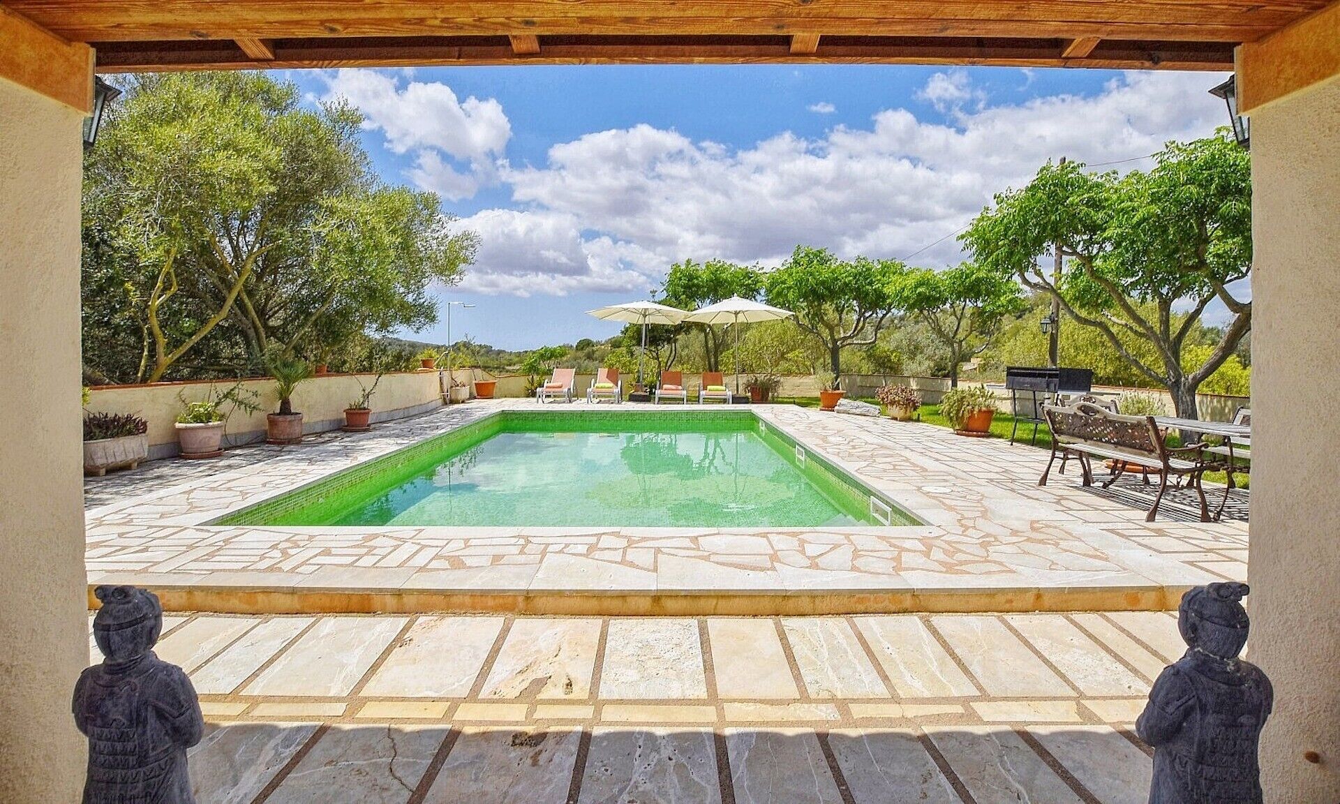 Une piscine dotée d’une terrasse carrelée, entourée de plantes en pot et de mobilier d’extérieur.