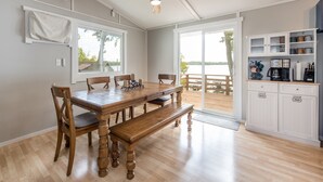 Un coin repas avec une table et des chaises en bois, un ventilateur de plafond et une vue sur une terrasse en bois, visible à travers des portes vitrées.