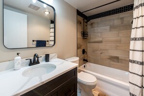 A modern bathroom with a white sink, black faucet, and a large mirror. There is a white toilet and a white bathtub with a shower curtain.