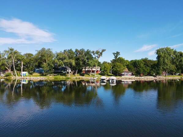 A lakeside view with a dock, boats, and houses along the shore.