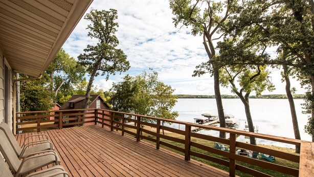 Une terrasse en bois avec des chaises, une rambarde et une vue sur un lac bordé d’arbres.