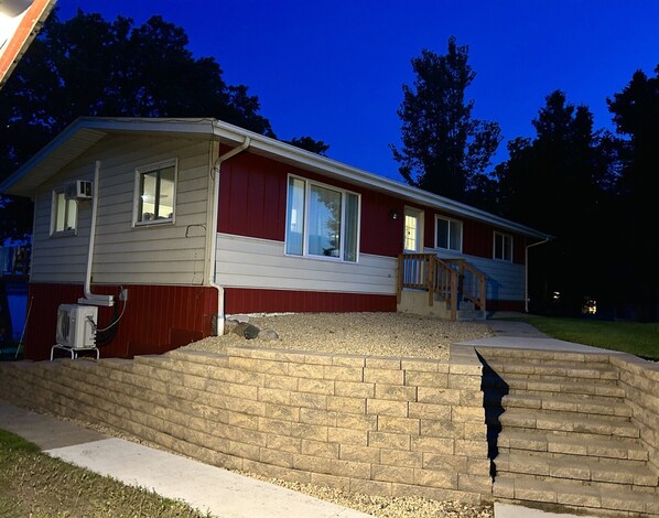 A two-story house with a red and white exterior, a front porch with a wooden staircase, and a brick retaining wall.