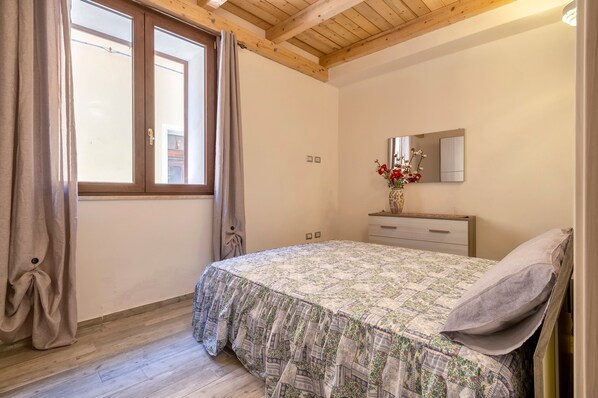 Ein Schlafzimmer mit Bett, Schminktisch, Spiegel und einem Fenster mit Vorhängen.