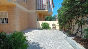 A courtyard with a paved walkway, a small fountain, and a building with a balcony. - House by the sea with large equipped garden (Torvaianica)