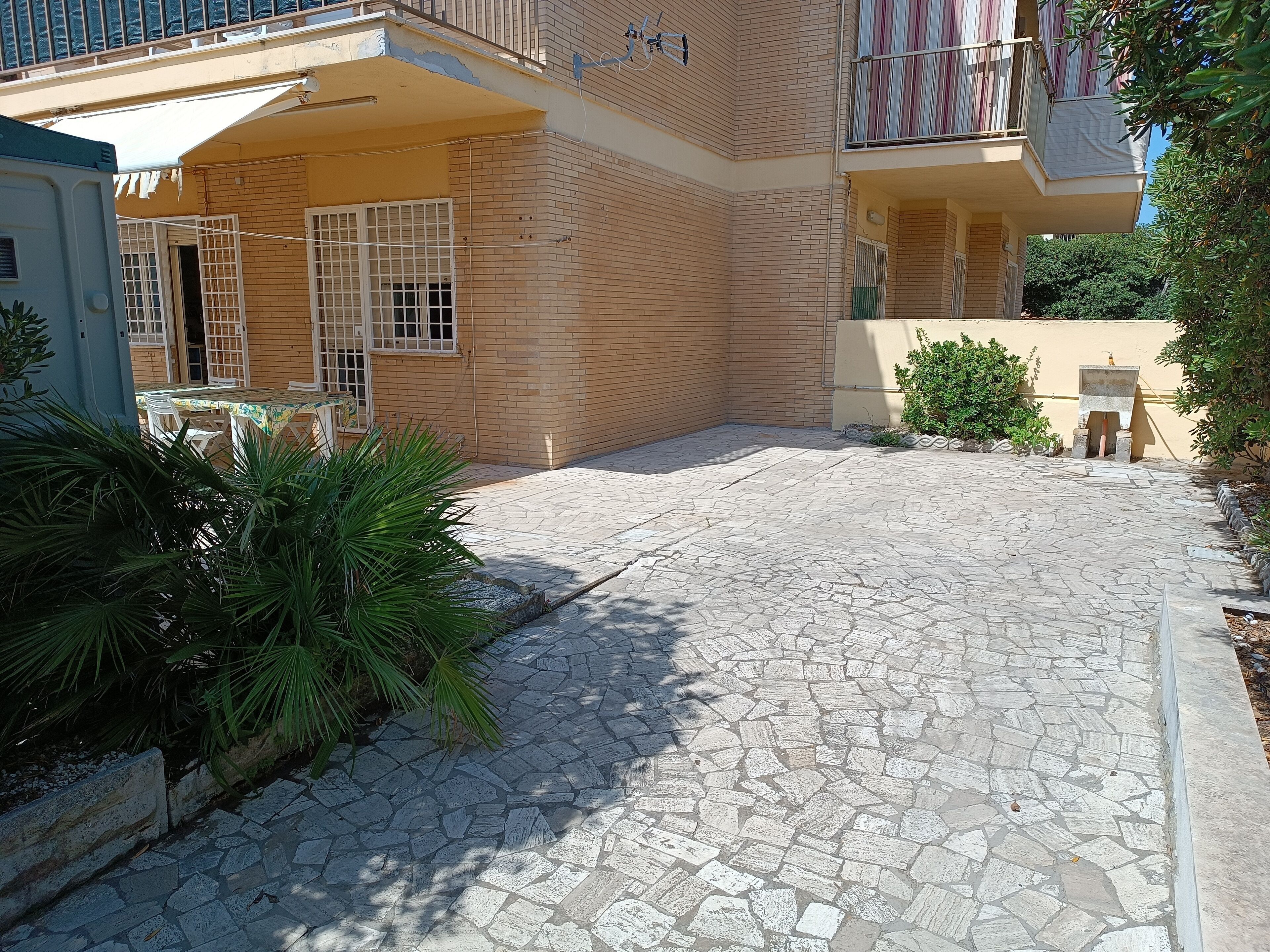 Une cour dallée de pierres, une petite fontaine et un balcon agrémenté d’un rideau à rayures.