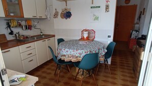 A compact kitchen with a dining area, featuring a tiled floor, wooden cabinets, and a small table with chairs. - House by the sea with large equipped garden (Torvaianica)