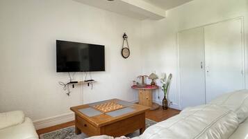 Un salon doté d’un téléviseur à écran plat, d’une table basse en bois, d’un canapé en cuir blanc et d’une petite table d’appoint agrémentée d’objets décoratifs.
