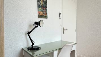 Un piccolo ufficio moderno con una scrivania in vetro, una sedia bianca, una lampada da scrivania nera e una porta con serratura a codice.