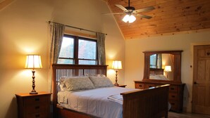 Una camera da letto con un letto di legno, due comodini con lampade, una ventola a soffitto, un'ampia finestra con tende e un armadio in legno.