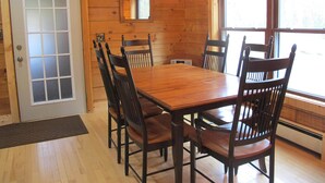 Una sala da pranzo in legno con un grande tavolo e sedie, un lampadario e ampie finestre.