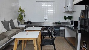 Cocina compacta con sofá, dos mesas, microondas y una cafetera SuCafe.