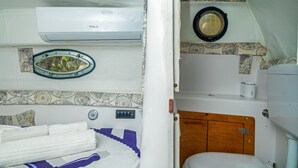 Ein kleines Zimmer mit einem Bett, einer Toilette und einer Wand-Klimaanlage.