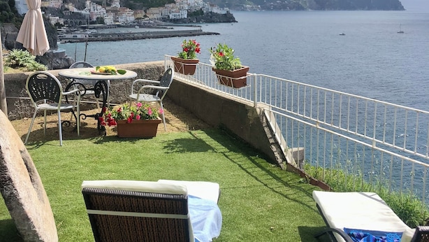 Eine Terrasse mit Meerblick, ausgestattet mit einem Tisch, Stühlen und Blumentöpfen.