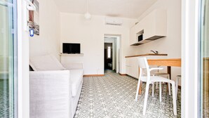 A modern, minimalistic living space with a patterned floor, a white sofa, a dining area with a wooden table and chairs, and a television mounted on the wall.