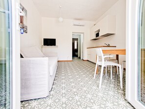 Un espacio habitable moderno y minimalista, con piso estampado, un sofá blanco, una zona de comedor con mesa y sillas de madera, y un televisor montado en la pared.