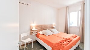 A bedroom with a bed, a chair, a nightstand, and a window.