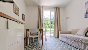 A room with a sofa, a dining table with chairs, a refrigerator, and patterned floor tiles.