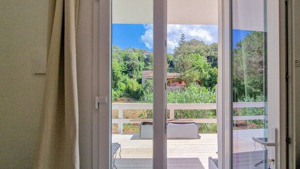 A sliding glass door leading to an outdoor deck with a white railing, a bench, and a small orange rug.