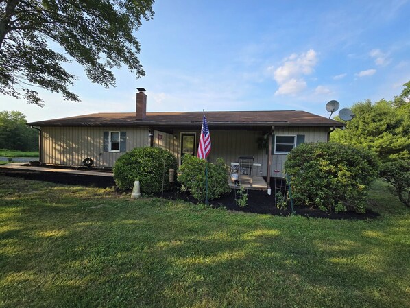 A single-story house with a front porch, an American flag, and satellite dishes.