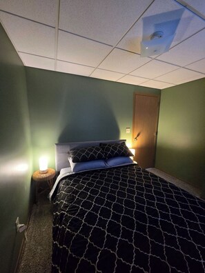 A bedroom with a bed, a nightstand, a wall socket, and a door.