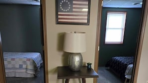 A room with a wooden floor, a table with a lamp, a framed American flag, and two beds. - Escape to Nature – 2 Bdrm Home on 13 Private Acres near ATV, SSRT trails and PSU (Munson)