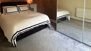 A bedroom with a brick wall, a large bed, a bedside table, a mirror, and a radiator. - The Luxury Annex at Barmby Moor House (York)